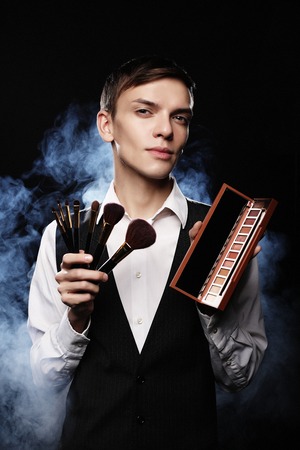 Young male make up artist posing with make-up brushes and shadowの写真素材