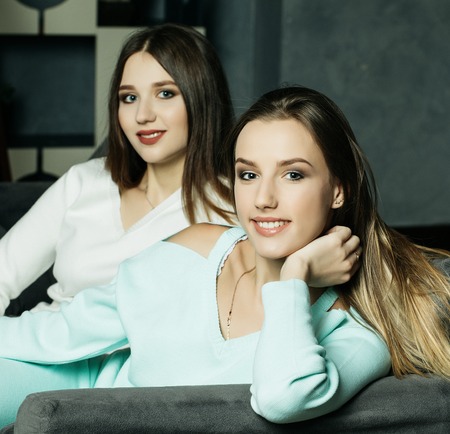 Two smiling friends sitting on the couch looking at camera in sitting room at homeの写真素材