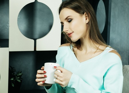 Beautiful and cute. Beautiful young woman holding coffee cup and  sitting on chair at home. Lifestyle concept.の写真素材