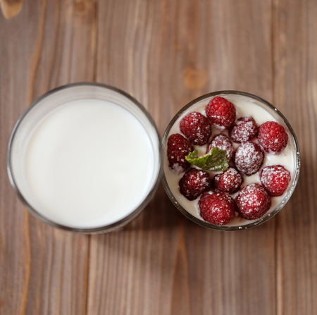 A glass of milk and granola with raspberries over wooden backgroの写真素材