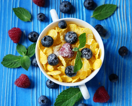 Healthy eating, food and diet concept - Cornflakes with berries raspberries and blueberries on blue...