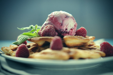 Waffles with raspberry ice cream and fresh raspberries, decorated with mint over blue wooden background, close upの写真素材