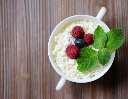 Cottage cheese with raspberries and blueberries in a bowl for healthy breakfast with ripe berries over rustic wooden background. Top view.の写真素材