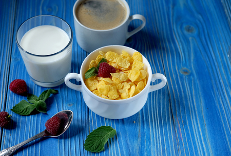 Healthy eating, food and diet concept - Cornflakes with berries, milk and coffee for breakfast. Blue wooden background.の写真素材