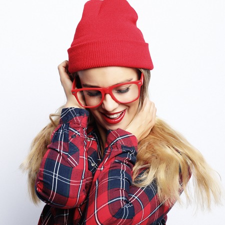Fashion studio portrait of pretty young hipster blonde woman with bright sexy make up and glasses , wearing stylish urban plaid shirt and red hatの写真素材