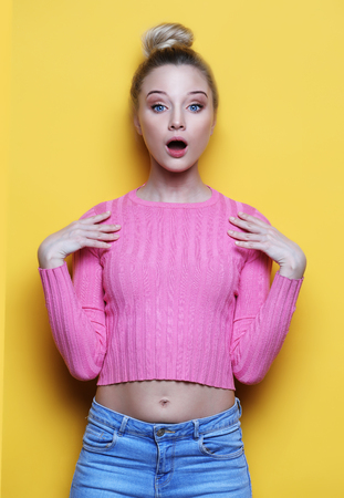Surprised young blond woman shouting over yellow background. Looking at camera.の写真素材