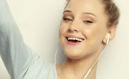 Blond girl in headphones listening music taking photo makes self portrait on smartphone wearing a casual clothesの写真素材