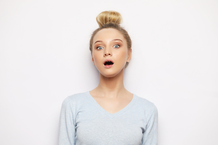 Indoor shot of stupefied shocked blonde woman keeps mouth widely opened, looks at camera, wears casual clothes, isolated over white background.の写真素材