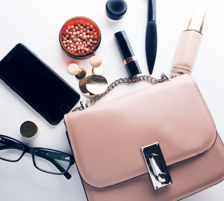 Flat lay of pink leather woman bag open out with cosmetics, accessories and smartphone on white background with copy space.の写真素材