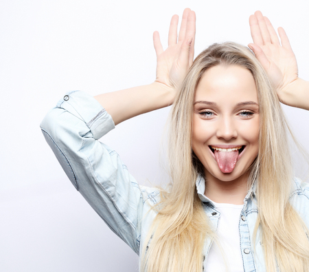 lifestyle and people concept: Look at me like Im funny. Portrait of a young beautiful girl on a white background with a smiling showing horns on the camera.の写真素材