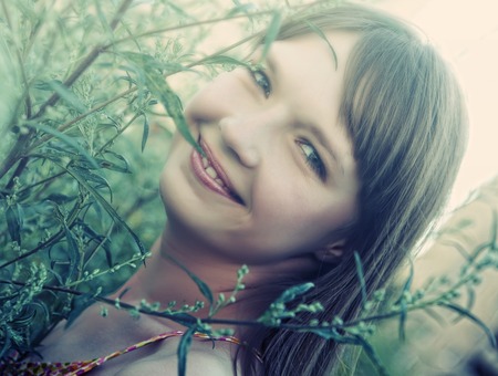 woman outdoors under green leaves.