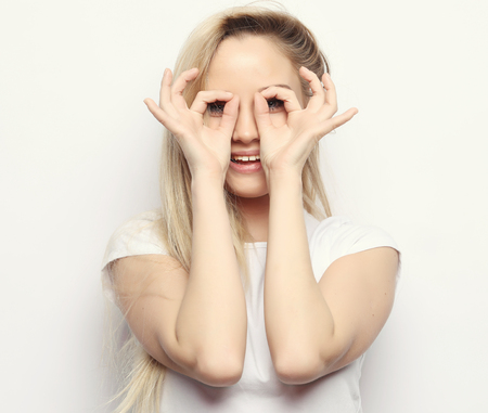 lifestyle and people concept - Happy excited young woman looking through hole made of her fingers over white backgroundの写真素材