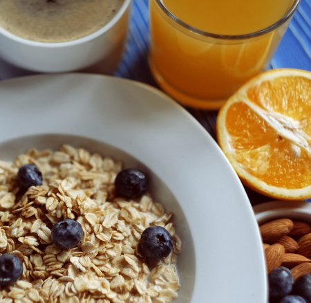 Oatmeal porridge with fresh blueberries, almonds, coffee and orange juice in white bowl on blue...