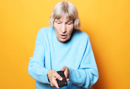 lifestyle and people concept: funny grandma is holding a TV remote over yellow backgroundの写真素材