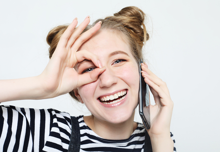 beautiful joyful woman smiling, demonstrating white teeth, looking at the camera through fingers in okay gesture.の写真素材
