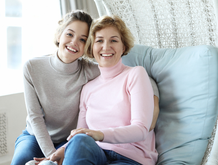 Beautiful senior mom and her adult daughter are hugging, looking at camera and smiling.の写真素材