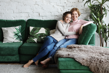 Beautiful senior mom and her adult daughter are hugging, looking at camera and smiling.の写真素材