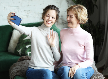 Portrait of beautiful mature mother and her daughter making a selfie using smart phone and smiling, home and happy.の写真素材