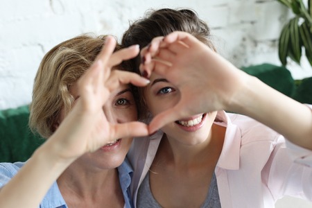 Mother and daughter love. Adult woman and young woman stacking hands in heart sign looking at camera.の写真素材