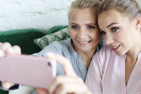 Portrait of beautiful mature mother and her daughter making a selfie using smart phone and smiling, home and happy.の写真素材