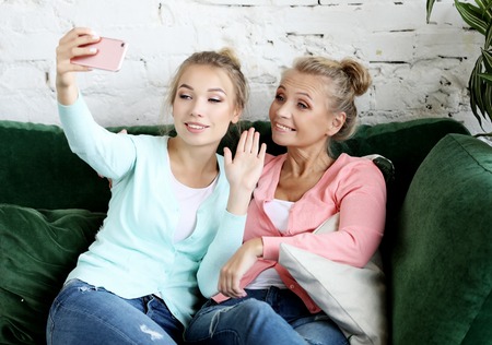 Portrait of beautiful mature mother and her daughter making a selfie using smart phone and smiling, home and happy.の写真素材
