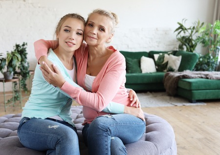Beautiful senior mom and her adult daughter are hugging, looking at camera and smiling.の写真素材