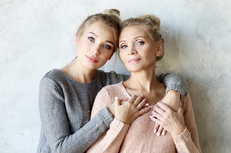 Beautiful senior mom and her adult daughter are hugging, looking at camera and smiling.の写真素材