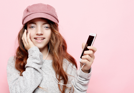 Joyful amazing little girl wearing pink listening to music with headphones isolated on pink background. Expressing brightful emotions to camera, enjoying lovely song.の写真素材