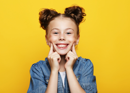 Portrait of cheerful smiling little girl on yellow backgroundの写真素材