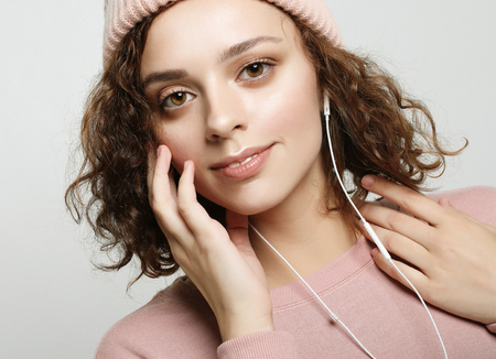 beautiful girl in headphones listens to music and smiles while standing on a white background in a pink sweatshirt and hat.の写真素材
