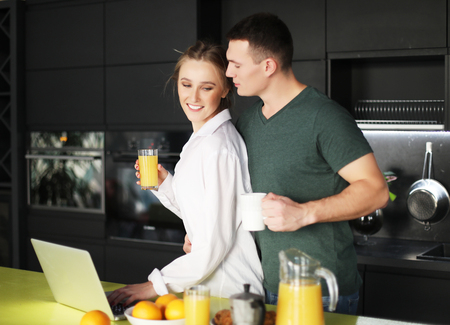 young couple at home having coffee in kitchen and working on laptop computerの写真素材