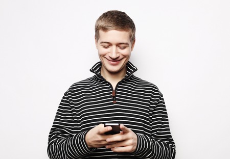 Happy young man in glasses typing sms on white backgroundの写真素材