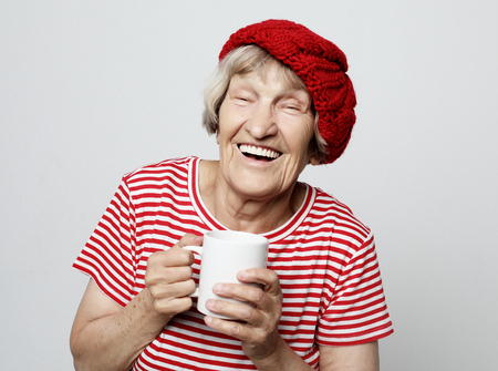 old excited lady smiling laughing, holding cup drinking coffee or teaの写真素材