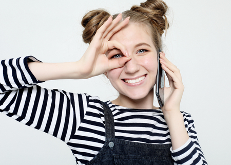 joyful woman smiling, demonstrating white teeth, looking at the camera through fingers in okay gesture.の写真素材