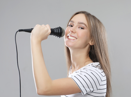 Beauty model girl singer with a microphone over light grey  backgroundの写真素材