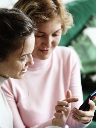 Family, people and technology. Aged woman and her adult daughter using smartphone at homeの写真素材