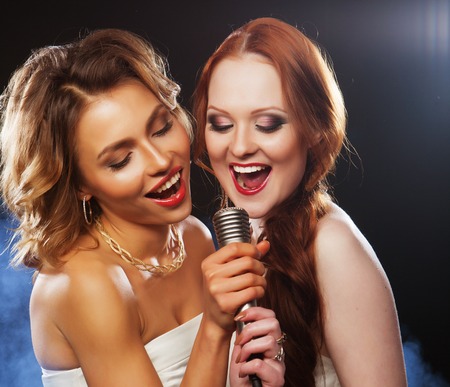 lifestyle, party and people concept - two beautiful stylish girls singing karaoke at the clubの写真素材