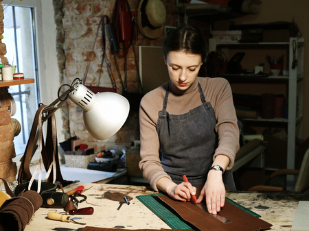 young woman works in a bag making studio, cuts out details