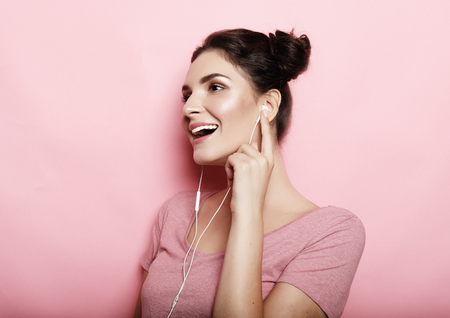 Beautiful young woman in headphones listening to music over pink backgroundの写真素材