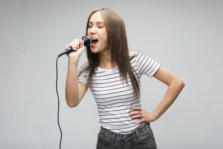 Beauty model girl singer with a microphone over light grey  backgroundの写真素材