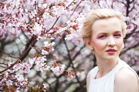 Portrait of a beautiful young blond woman on a background of pink cherry blossoms in springの写真素材