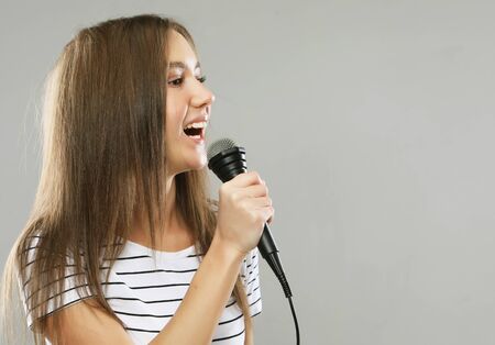 Beauty model girl singer with a microphone over light grey  backgroundの写真素材
