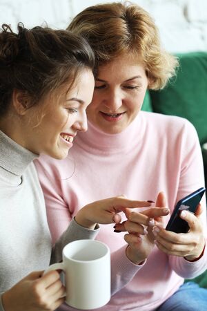 Family, people and technology. Aged woman and her adult daughter using smartphone at home.