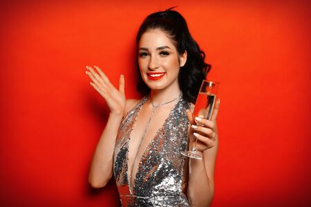 Young attractive woman evening dress holding glass of champagne over red background.の写真素材