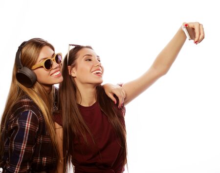 tehnology, emotion and people concept: happy best girlfriends making selfie on smartphone over white backgroundの写真素材