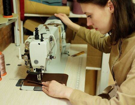 Closeup on young woman sewing leather handbag