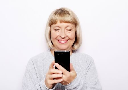 Lifestyle, tehnology and people concept: Smiley senior woman is holding a new smartphone in her...