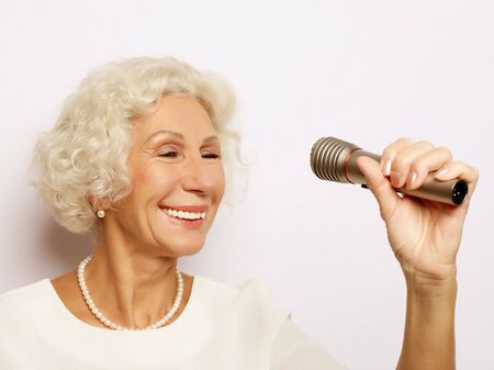 lifestyle and people concept: Portrait of charming modern grandmother holds up the microphoneの写真素材