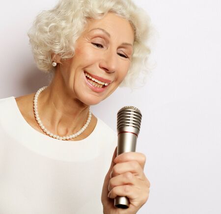 lifestyle and people concept: Portrait of charming modern grandmother holds up the microphone stand and singsの写真素材