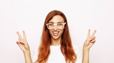 Portrait of gorgeous woman looking at camera with smile and showing peace sign with fingersの写真素材
